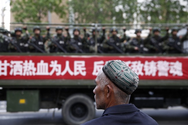A Uighur man looks on as a truck carrying paramilitary policemen travel along a street during an anti-terrorism oath-taking rally in Urumqi