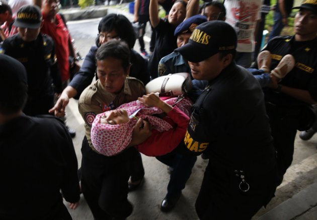 Government security officials carry family member of passengers onboard AirAsia flight QZ8501 after she collapsed at a waiting area in Juanda International Airport