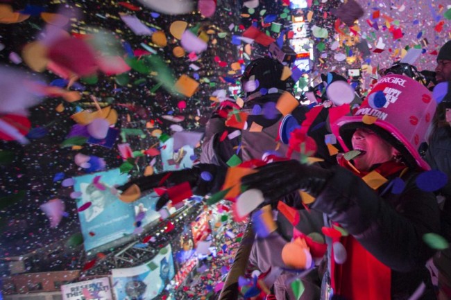 Revellers toss confetti over Times Square from a hotel balcony as the clock strikes midnight during New Year's Eve celebrations in New York