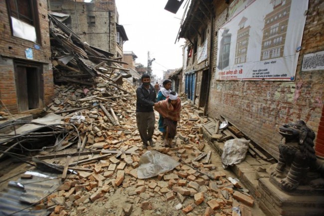 An elderly injured woman is taken home through earthquake debris after treatment in Bhaktapur near Kathmandu, Nepal, Sunday, April 26, 2015. A strong magnitude 7.8 earthquake shook Nepal's capital and the densely populated Kathmandu Valley before noon Saturday, causing extensive damage with toppled walls and collapsed buildings, officials said. (AP Photo/Niranjan Shrestha)