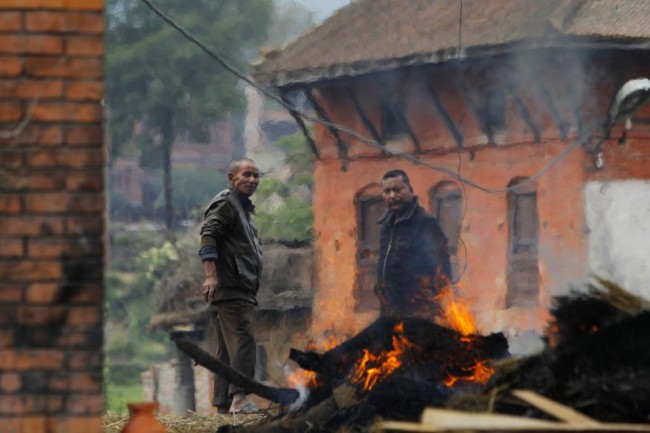 Nepalese people stand beside the funeral pyre of a family member who died in Saturday's earthquake in Bhaktapur, Nepal, Sunday, April 26, 2015. A powerful, magnitude 6.7 aftershock shook the Kathmandu area of Nepal on Sunday, a day after the massive earthquake devastated the region and destroyed homes and infrastructure. (AP Photo/Niranjan Shrestha)