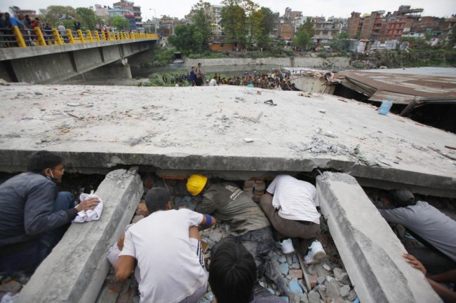 Rescuers look for victims under a building that collapsed after an earthquake  in Kathmandu, Nepal, Saturday, April 25, 2015. A strong magnitude-7.9 earthquake shook Nepal's capital and the densely populated Kathmandu Valley before noon Saturday, causing extensive damage with toppled walls and collapsed buildings, officials said. (AP Photo/ Niranjan Shrestha)