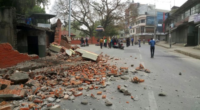 People gather in an intersection near a damaged building in Kathmandu, Nepal, Saturday, April 25, 2015. A strong magnitude-7.9 earthquake shook Nepal's capital and the densely populated Kathmandu Valley before noon Saturday, causing extensive damage with toppled walls and collapsed buildings, officials said. (AP Photo/Tashi Sherpa)